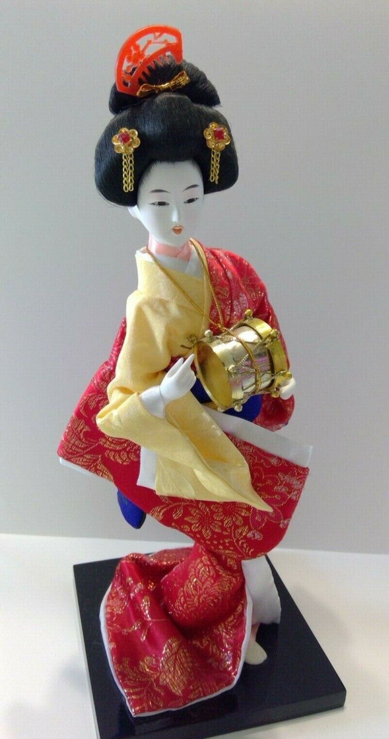 Geisha figure dressed in red, yellow, blue, and gold holding a drum.