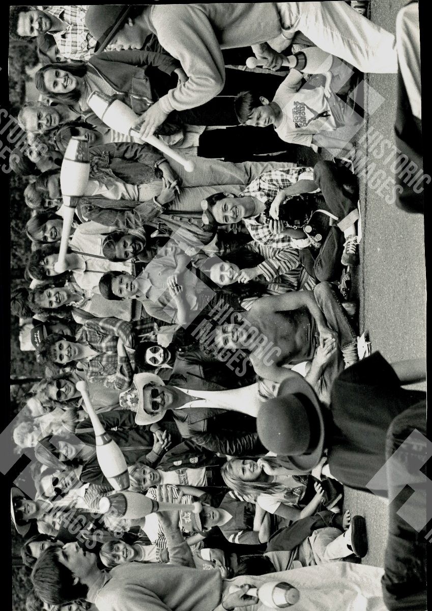 1983 Crowd of people are gathered around a man performing a juggling act 1983 Crowd of people are gathered around a man performing a juggling act