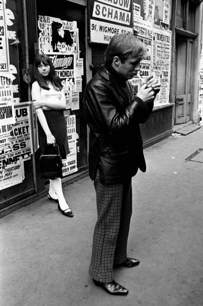 British young man lighting a cigarette Behind him a wall covered p- Old Photo