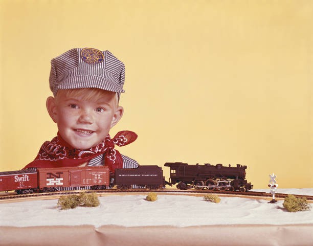 Boy standing by miniature train smiling Historic 1960s Old Photo