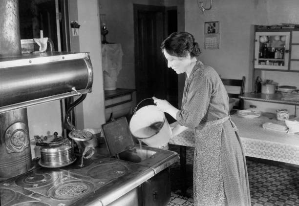 Woman in a kitchen pours water into a stove 1940s Historic Old Photo