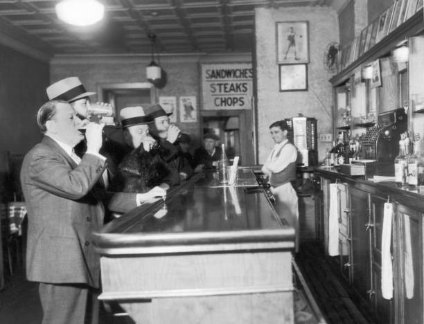 Four men drink at counter of a bar while bartender looks with his a- Old Photo