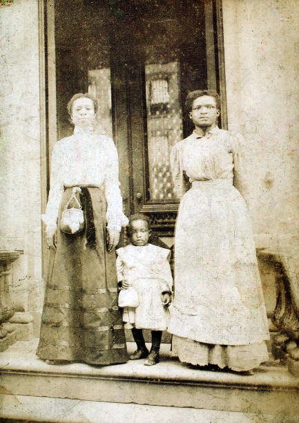 Two women a child standing on step in front of a doorway of a hous- Old Photo