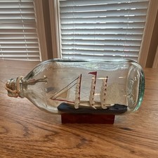 A decorative miniature ship in a glass bottle mounted on a red wooden base. picture